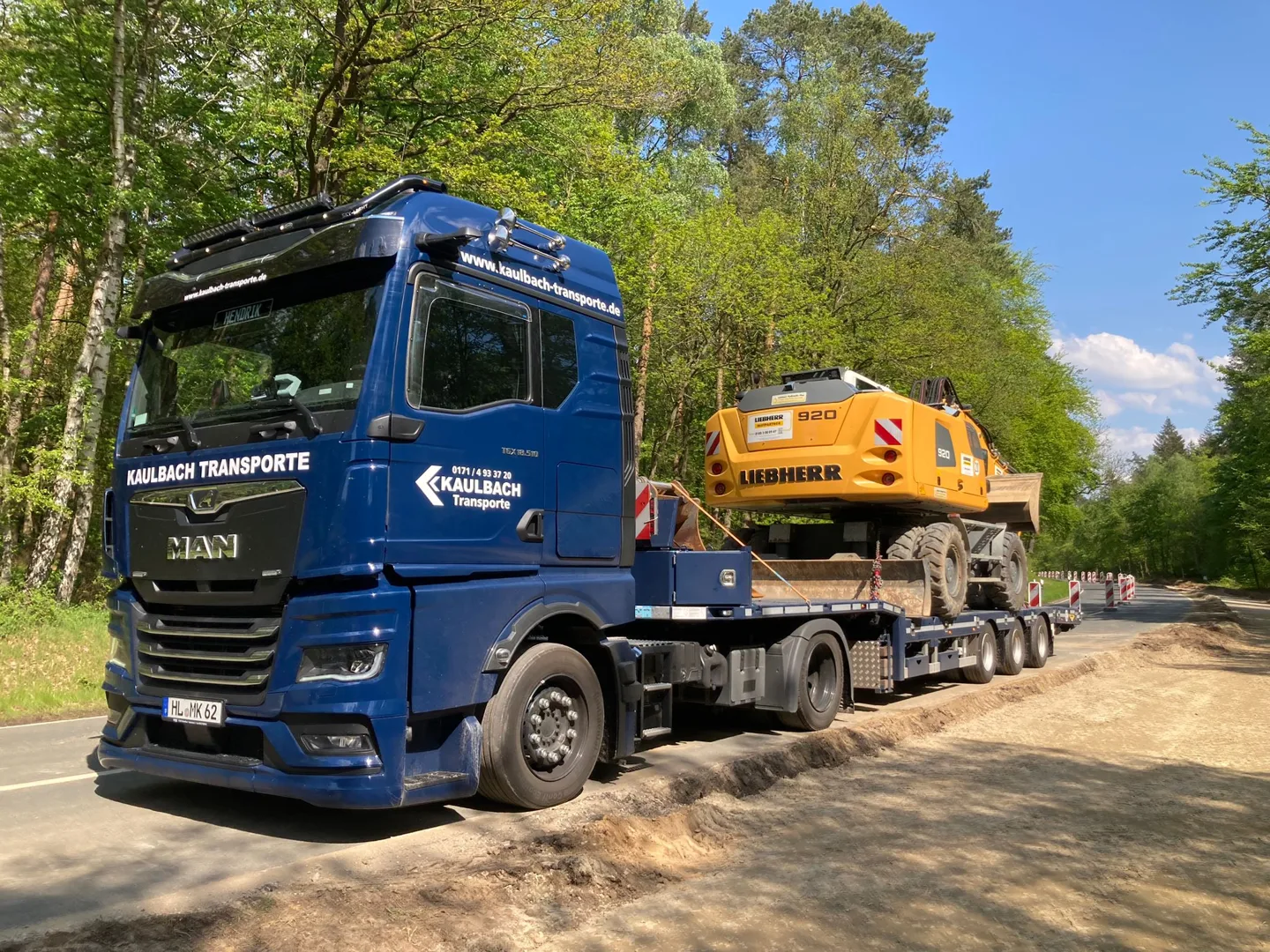Blauer Kaulbach MAN mit Baumaschine an einem sonnigen Tag im Grünen